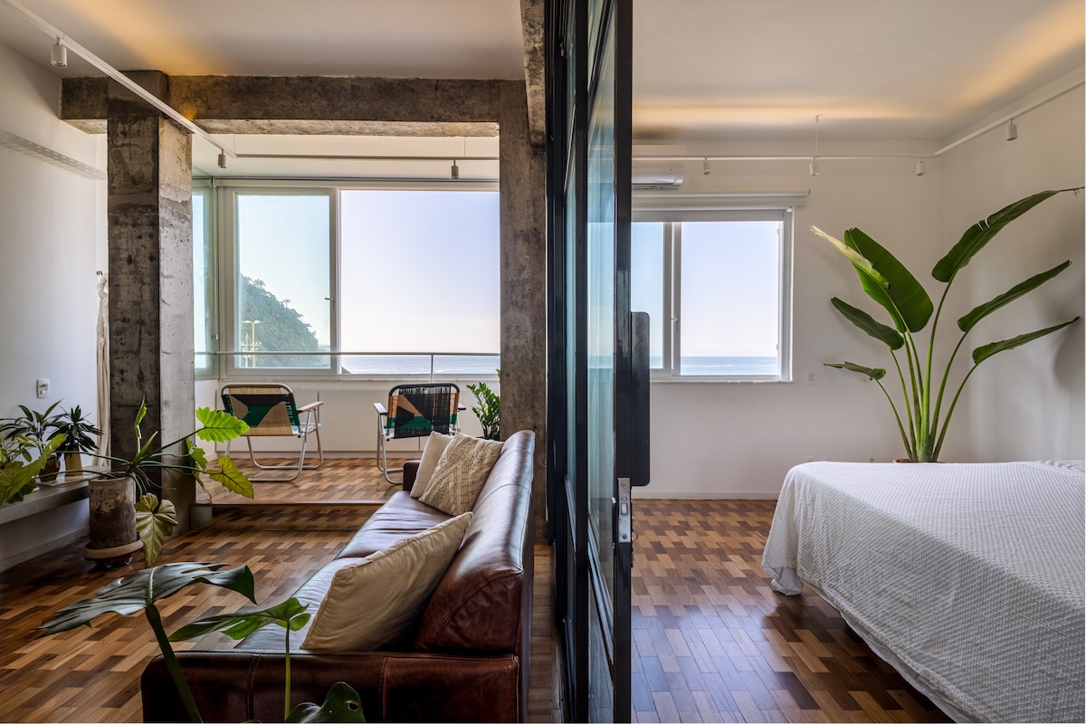 Sala e quarto integrados com colunas de concreto aparente e piso de madeira