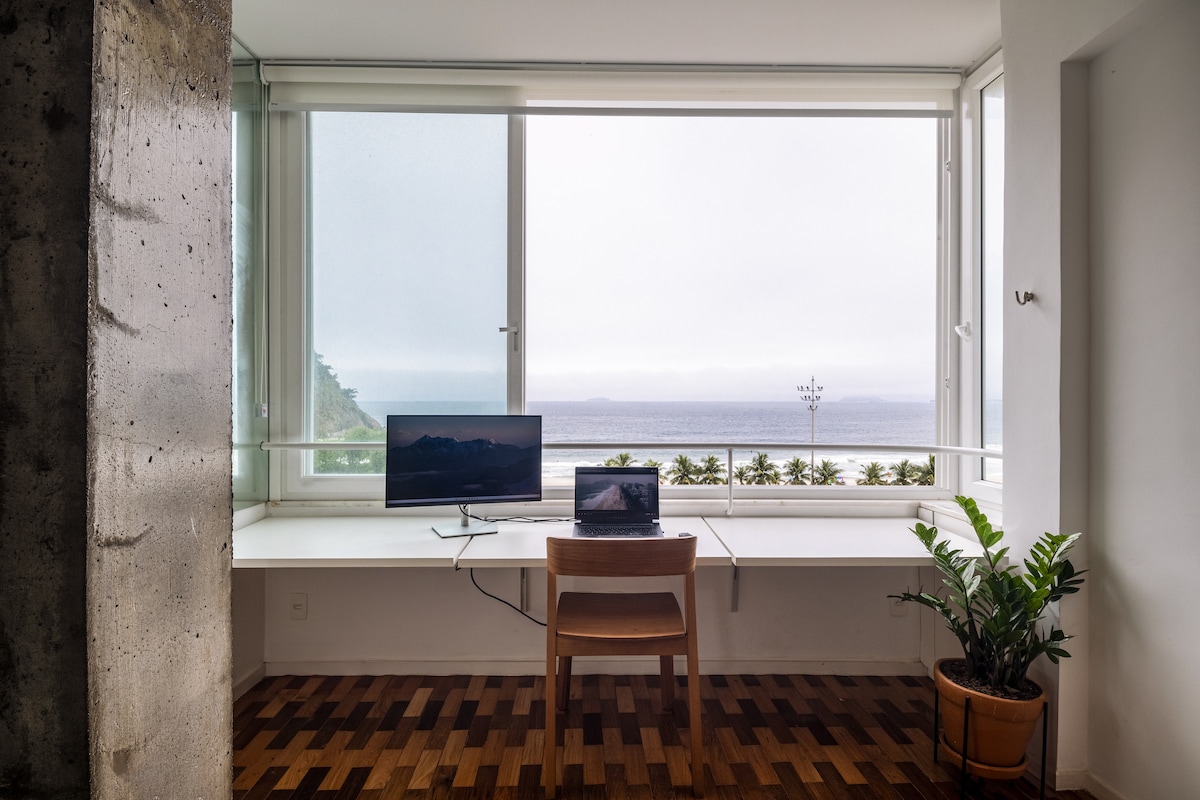 Escritório com mesa de pé e cadeira de madeira de frente para a praia